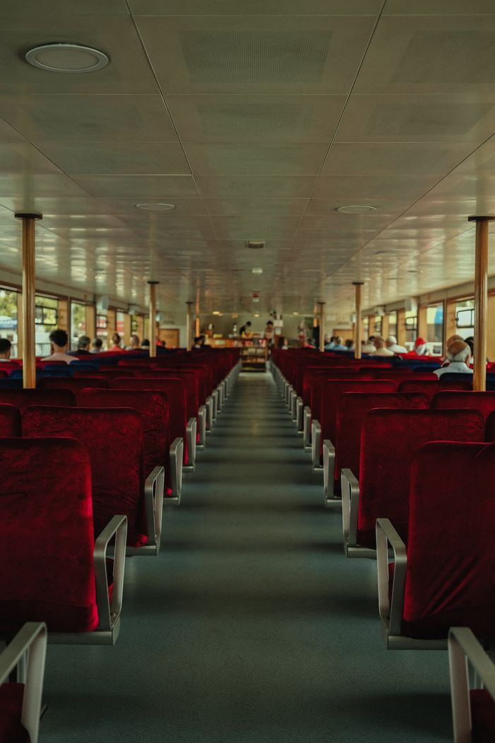 collection-05 Symmetrical view inside a passenger ferry with empty red seats and peaceful atmosphere.